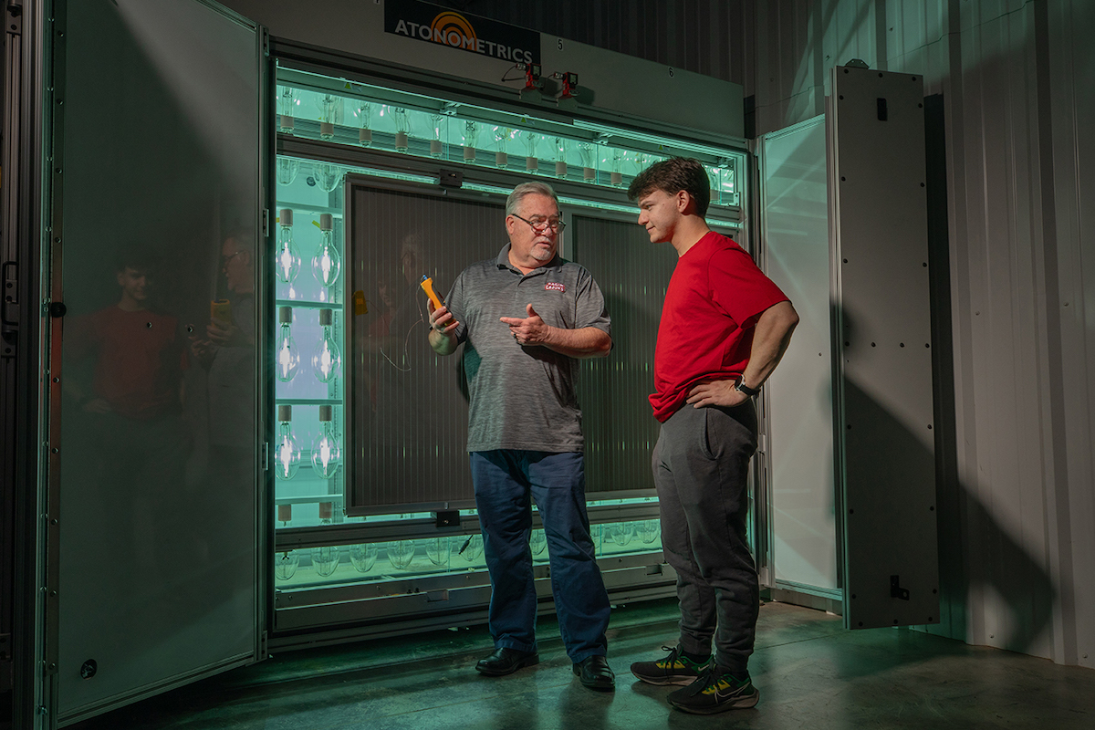 Dr. Terrence Chambers and student Wyatt Stoute standing in front of a solar testing chamber.