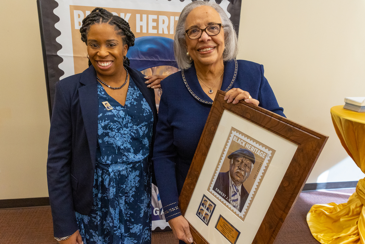 Cheylon Woods, left, director and archivist of the Ernest J. Gaines Center at UL Lafayette, is seen with Dianne Gaines, the author’s widow, holding a framed commemorative copy of the Ernest Gaines stamp.