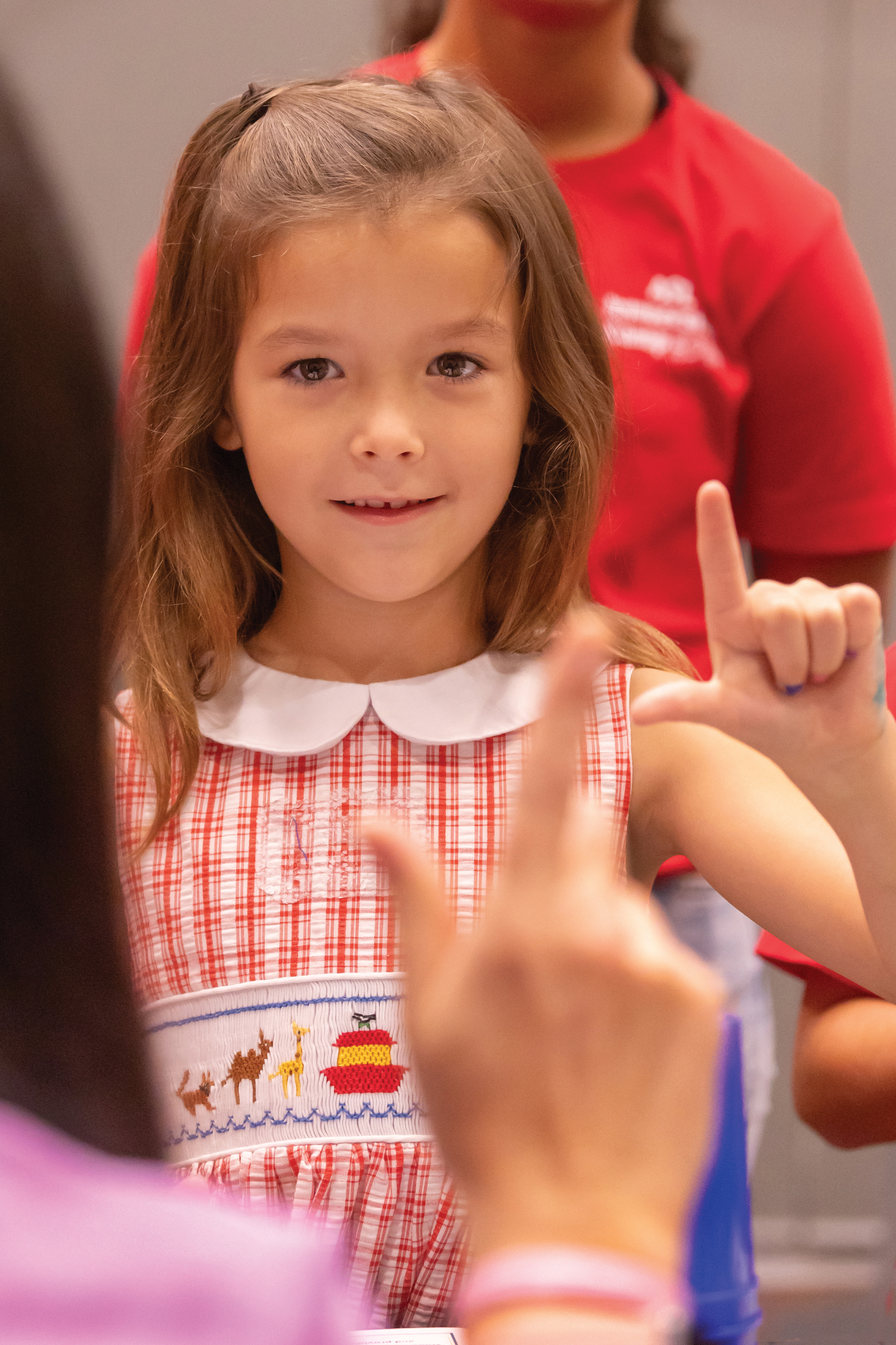 Young girl with brown hair makes an "L" with her hand during an ASL summer camp.