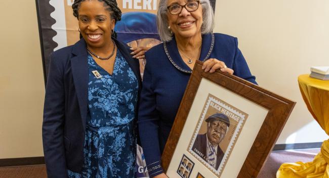 Cheylon Woods, left, director and archivist of the Ernest J. Gaines Center at UL Lafayette, is seen with Dianne Gaines, the author’s widow, holding a framed commemorative copy of the Ernest Gaines stamp.