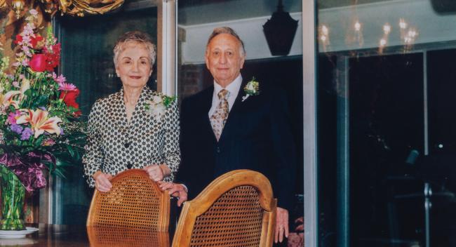 A couple stands next to a bouquet of flowers sitting on a wooden table.