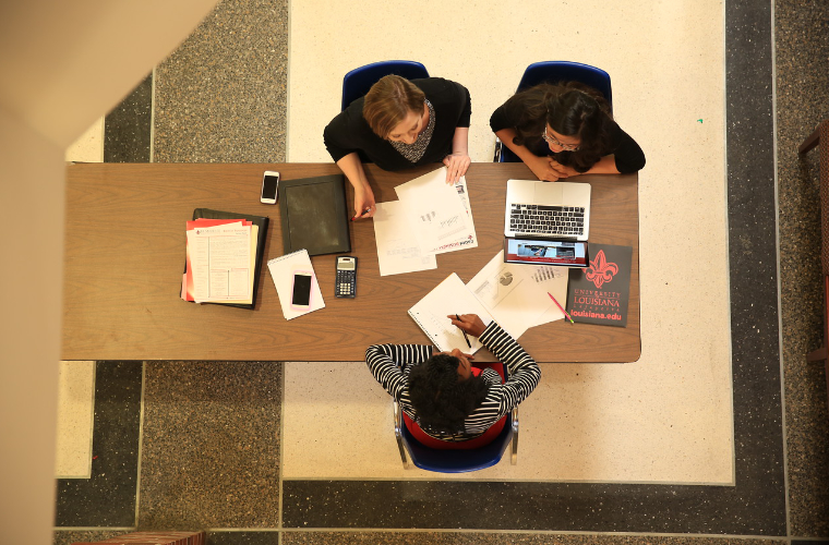 Three UL Lafayette students viewed from above while working at a table among notes and laptops