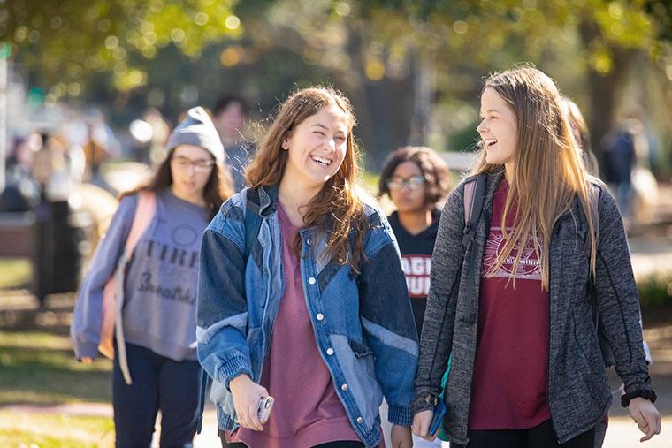 Two University of Louisiana at Lafayette female students smile and laugh while walking on campus