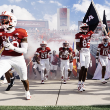 A group of UL footballs strut onto the field while carrying flags